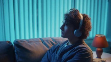 Genç adam geceleri kulaklıkla koltukta oturur, müzik dinler ve dinlenir. Duygusal Denge ve Zihinsel Refah İçin Akşam Ritüeli. Farkındalık, Ses Terapisi, Dijital Sakinlik.