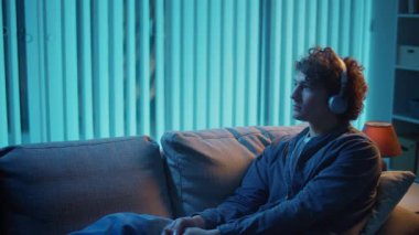 Genç adam geceleri kulaklıkla koltukta oturur, müzik dinler ve dinlenir. Duygusal Denge ve Zihinsel Refah İçin Akşam Ritüeli. Farkındalık, Ses Terapisi, Dijital Sakinlik.