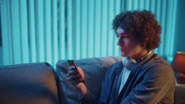 Man, Kanepe Kaydırma Telefonunda Rahatlıyor, Muhtemelen Podcast veya Browsing dinliyor. Günlük Kişisel Bakım ve Dijital Çağ 'da Yavaş Yaşam. Dijital Detox, Akıl Sağlığı, Odaklanma Kipi.