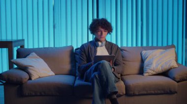 Man, Tablet Kullanarak Koltuğa Rahatlar, Muhtemelen Okuma ve Yayınlama İçeriğini İzler. Günlük Kişisel Bakım ve Dijital Çağ 'da Yavaş Yaşam. Dijital Detox, Akıl Sağlığı, Odaklanma Kipi.