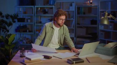 Proje Planlama. Odaklanmış Profesyonel Adam Planları Analiz Ediyor ve Gece Dizüstü Bilgisayar Üzerinde Çalışıyor. Mimarlık, Mühendislik, İş Stratejisi ve Kariyer Geliştirme Konsepti.