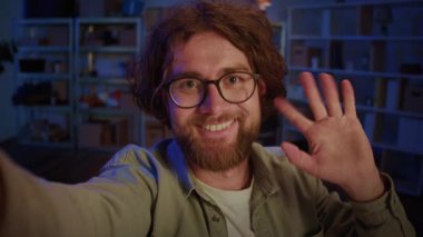 Kameraya bakan ve video görüşmesinde el sallayan gözlüklü gülen adam. Çevrimiçi Karşılama, Uzaktan İletişim, Dijital Bağlantı, Sanal Buluşma ve Dostça Giriş.