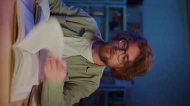 Genç adam, Yoğun Gece Çalışması sırasında bir kitabın sayfalarını çeviriyor. Dikey video. Öğrenme, Araştırma, Bilgi Keşfi, Sınav Hazırlığı ve Stres ve Konsantrasyonla Akademik Odaklanma Konsepti.