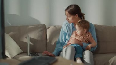 Kadınlar Başarıyı Yeniden Geliştiriyor. Annesinin kucağında yürümeye başlayan çocuğu tutarken uzaktan kumandayla iş, sağlık ve annelik dengesini gösterdiğinden emin.