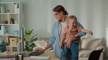 Yeni ofis olarak eve. Genç Anne, Ağlayan Bebek 'i tutarken Uzaktan Çalışmayı Dengeliyor, Aile Yaşamı ve Modern Çalışma Kültürünün Zorluklarını Gösteriyor