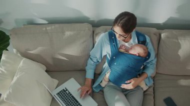 Melez Ebeveynlik. Genç Anne 'nin bebek taşırken dizüstü bilgisayar kullanması, ebeveynliği ve uzaktan çalışmayı bir arada tutması