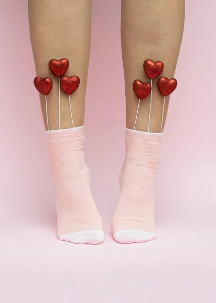 Red hearts in pink women\'s socks. Valentine\'s Day love concept on pink background. Minimal romantic idea.