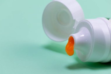 white toothpaste container, orange toothpaste on a light green background