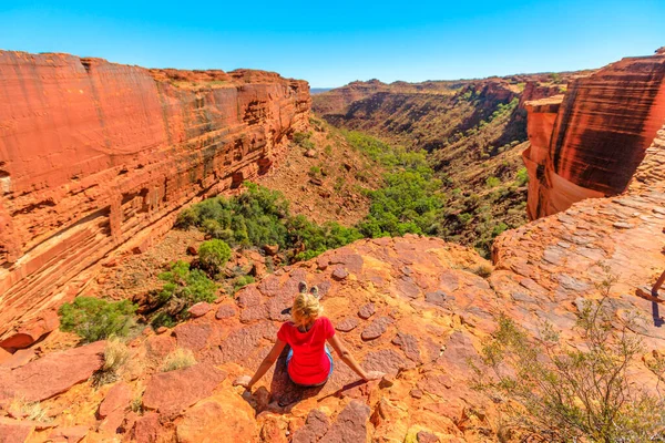 woman on the edge of Kings Canyon in Watarrka National Park, Australias Red Center. rest after trekking on Rim Walk by the canyon edge in Northern Territory of Australian Outback.