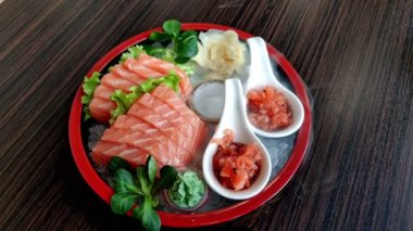 Somon balığı, zencefil, wasabi ve sebzeli sashimi tabağı ahşap bir masada düz bir görünüm sergiliyordu. Çiğ somon balığı parçaları Japon yemek tarzında taze kesilmiş. Japon füzyon yiyeceği..