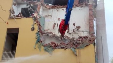 İnşaat alanındaki bir yapıyı yıkmak için kullanılan mekanik kürek ve bir evin yenilenmesi inşaat sektörünün bir parçası. Erkekler, duvarları yıkmak için bir buldozer kazıcısı kullanırlar..