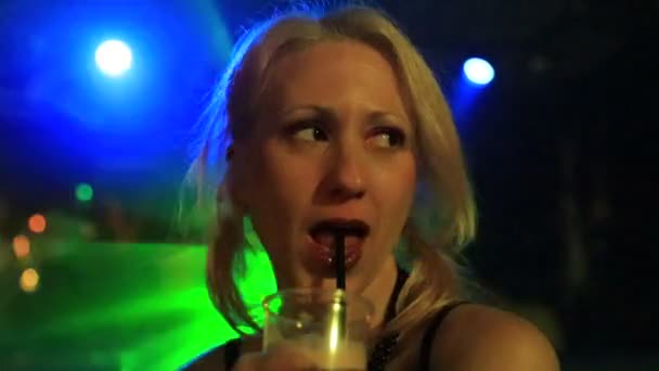 一位漂亮的金发女性正在蓝绿色激光闪光灯下 在灯光昏暗的舞厅里喝着一杯混合饮料 晚上的娱乐 还有成年人的生活方式 沉迷于慢动作 — 图库视频影像