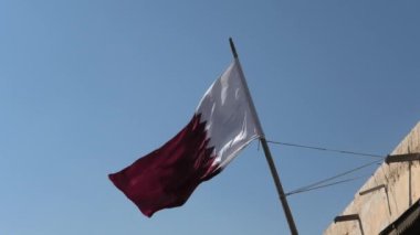 A Qatar flag fluttering against a cobalt sky. In the Persian Gulf region of the Middle East.