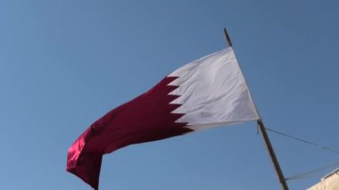 Against the backdrop of a clear blue sky, a flag belonging to Qatar country is situated in the Middle East, in the Persian Gulf region.