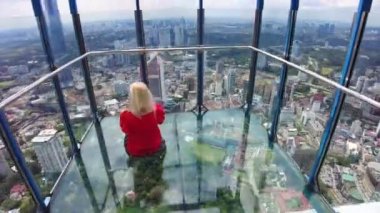Kız, Kuala Lumpur gökyüzünde cam bir köprüde yalınayak duruyor. Bu kısacık an için, zamanın ve uzayın endişelerinden ve kendisiyle ve etrafındaki dünyayla barıştan kurtuldu..