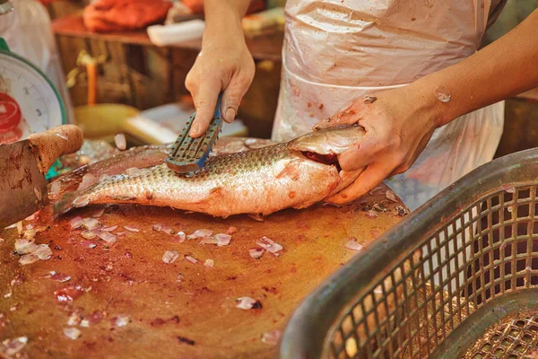 close-up shot of a fishmonger scaling the fish up the fish in a Chow Kit Road Market stall in Kuala Lumpur. This bustling market is bustling with commercial activity and shoppers.