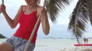 Ağır çekimde yaz tatili: Seyşeller 'in Praslin' indeki Anse Volbert Cote dOr plajında hindistan cevizi palmiyelerinin altında salıncakta sallanan bir kadın. Konum Chauve Souris adacığını da içerir..