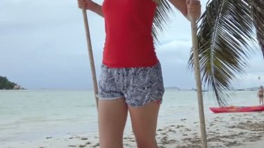 Anse Volbert Cote 'da, Praslin of Seychelles plajında, hindistan cevizi palmiyelerinin altında salıncakta sallanan ayak bilekliği olan bir kadın. Chauve Souris Adası, ve bunun arkasındaki fikir bir yaz tatili konsepti..