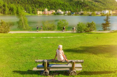 İsviçre 'deki St. Moritz Gölü' nün yanındaki St. Moritz parkında oturan turist kadın. Maloja bölgesindeki Grisons Kantonu 'ndaki St. Moritz göl kenarı.