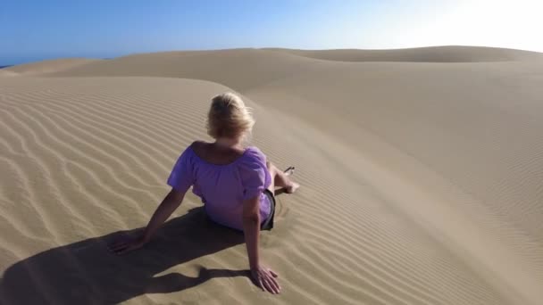 在大加那利亚的马斯帕洛马斯沙丘 女人坐在那里晒黑 感觉到阳光温暖在她的皮肤上 感觉到脚下沙子的柔软质感 她闻到了盐水的味道 听到了附近大海的声音 — 图库视频影像