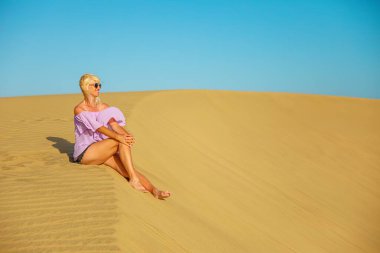 Gran Canaria 'nın Maspalomas Kumulları' nı ziyaret eden bir turist kadın yakınlardaki Maspalomas Sahili 'nde güneşleniyor ve dinleniyor..