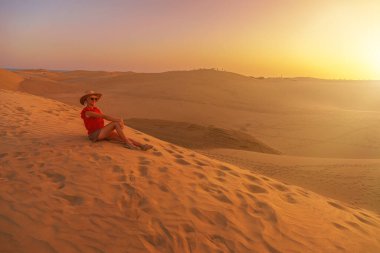 Kadın turist Maspalomas Kumulları 'nda güneş şapkası takıyor ve ya Gran Kanarya' nın Maspalomas Kumulları 'ndaki okyanus dalgalarını dinlemekten hoşlanıyor. Kum tepelerinin rüzgarda savruluşunu izlerken gözleri kapalıydı..