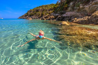Kadın Covid-19 sırasında cerrahi maskeyle Fetovaia sahilinde ve kristal denizde yüzüyor. Sarışın turist Coronavirus karantinasında Elba adasında banyo yapıyor. COVID salgını İtalya 'da tatil.