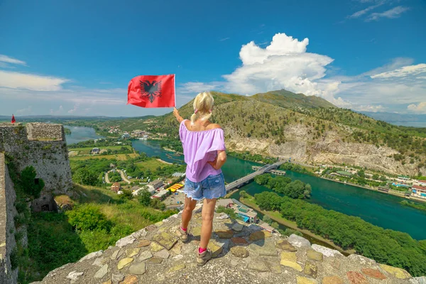 Woman holding Albanian flag at Rozafa castle in Albania. Castle provides breathtaking panoramic views of the surrounding terrain including Buna, Drin, and Kir rivers.
