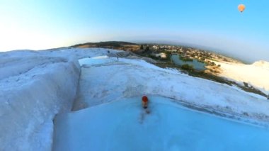 Pamukkales 'in berrak sularına batmış turist bir kadın saf mutluluğa doğru doğal havuzlara daldı. Sürrealist beyaz teraslarla çevrili Türkiye 'deki rahatlatıcı termal pınarların sıcaklığıyla kucaklanmış halde yüzüyor..