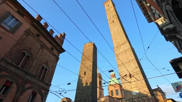 イタリアのボローニャの象徴的な2つのタワー 青空に対するシティーエンブレム アシネリとガリゼンダタワーは歴史的な街の中心に立っており ポルタ ラヴァナ広場の時計塔が時代を超越した魅力に加わっています — ストック動画