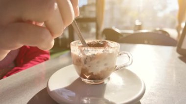 Bir İtalyan kafe barının masasında kaşıkla karıştırılmış bir fincan kapuçino. İnsanlar şafakta İtalyan kahvaltısı yapıyor. İtalyan yaşam tarzı. Yavaşlama Hareketi