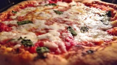 Domatesli Margherita pizza, mozzarella peyniri ve fırında fesleğen yaprağı. Daha yakından bakınca, kaynayan sosun üzerine ekstra saf zeytinyağı döküldüğünü görüyoruz. Geleneksel bir İtalyan tarifinden geliyor..