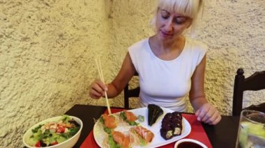 Zarif kadın somon balığı sashimi ve çubuklu Uramaki böreğini sever. Asya aromalı bir suşi barında. Sağlıklı bir yaşam tarzını hafif ve besleyici yemeklerle kucaklamak.