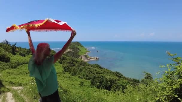 ブロンドの少女は アルバニアのロドン岬に誇らしげにアルバニアの旗を掲げています 岬に沿った穏やかなビーチは 平和的なリラックス 太陽を浸す機会を提供しています — ストック動画