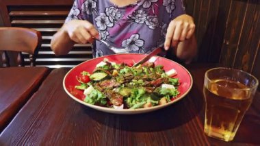 Kadın, orta pişmiş, ağız sulandıran pembe bir merkezi ve karamelize bir dışı olan biftek yiyor. Bu da onu her yemek için nefis bir süs eşyası yapıyor. Salata ve kırmızı birayla servis edilir.