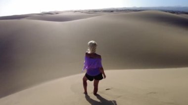 Gran Canaria 'nın Maspaloma Kumulları' nı ziyaret eden turist bir kadın rahat kıyafetler ve kumda yürümek için uygun ayakkabılar giyiyor..