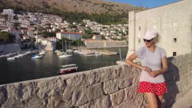 Hırvatistan 'ın Dubrovnik şehrinin üst duvarlarında eski bir ortaçağ limanına benzeyen bir kadın görülüyor. Dalmaçya 'nın tarihi Hırvatistan kenti Dubrovnik. UNESCO Venedik mimarisi. Arka planda Fort Lovrijenac kalesi.