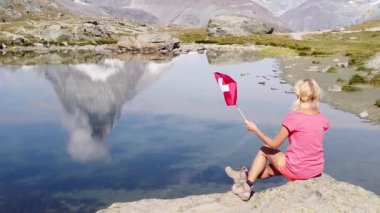 Matterhorn Dağı veya Mont Cervin 'de İsviçre bayrağı taşıyan kadın Riffelsee Gölü' ne yansıdı. Zermatt 'ta turizm, Valais Kantonu, İsviçre. Popüler turist cazibesinin manzarası