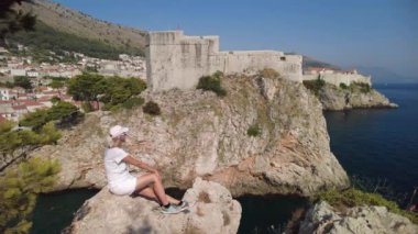 Batı limanındaki Lovrijenac kalesinde dinlenen bir kadın. Hırvatistan 'daki Bokar Kalesi ile Dubrovnik şehir manzarası. Dalmaçya 'nın tarihi kenti ve UNESCO Dünya Mirası Alanı.