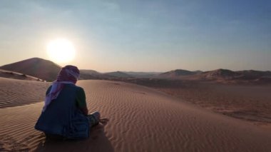 Şafak vakti altın kuma zıt kefiah şapka ile Boş Mahalle 'nin uçsuz bucaksız adamı. Umman Rub al-Khali çölünde macera ve yalnızlık arıyor..