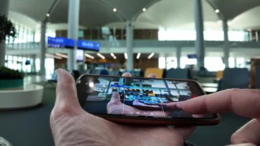 Havaalanı bekleme alanı terminalinin içini gösteren bir kamera görüntüsünü gösteren akıllı telefonu tutan el. Havaalanı salonundaki kablosuz bağlantı..