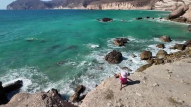 Turist bir kadın, Salalah 'taki El Fizayah Sahili' ni keşfediyor. Tertemiz beyaz kıyılar, şeffaf gök mavisi sular ve Umman 'daki nefes kesici Salalah dağları keşfedilmemiş bir cennet..