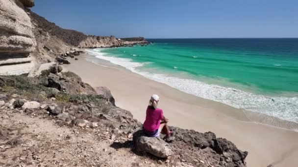 坐在阿曼萨拉拉Al Fizayah海滩的女游客 Fizayah隐藏在白沙滩上的海滩 面对令人敬畏的海岸 与清澈的海水相遇 — 图库视频影像