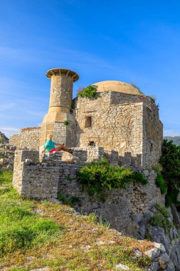 Arnavutluk 'taki Borsh Kalesi' ni heyecanlı bir şekilde keşfeden bir kadın turist, uzak sahillere bakan surlarda duruyor. Dalgaların kıyıya çarpma sesi.