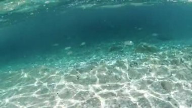 Suyun sakin sualtı manzarası, berrak mavi sudan İtalya 'nın Elba adasındaki çakıllı bir deniz tabanına süzülen güneş ışığı. Toskana takımadaları deniz rezervi ve Fetovaia plajı.