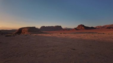 Durgun hareket hızı, güneşin Wadi Rum 'un engebeli dağlarının ardında batışını, uçsuz bucaksız Ürdün çölünü ılık, altın renklerde engin bir alacakaranlık gökyüzünün altında yıkamasını yakalar.