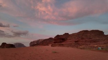 Ürdün 'ün Wadi Rum çölünde, sıcak bir günbatımı gökyüzü altında Jabal Al Qattar kaya oluşumunun büyüleyici görüntüsü manzaranın sükunetini ve güzelliğini yansıtıyor.