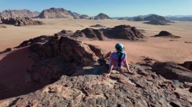 Turist kadın, Ürdün 'deki görkemli Wadi Rum çölüne tepeden bakan panoramik bir günbatımı sırasında Al Ghuroub' un huzur dolu güzelliğini yaşıyor.