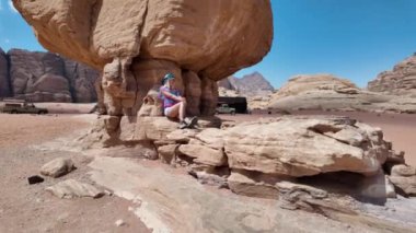 Turist kadın Wadi Rum Çölü 'ndeki ünlü Mantar Kayası' nın altında duruyor. Parlak mavi gökyüzü altında doğal kumtaşı oluşumunun güzelliğini ve ölçeğini gözler önüne seriyor.