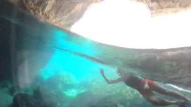 Kız, sakin bir mağara havuzunun berrak turkuaz suyuna dalıyor ve Elba Adası 'nın Mavi Mağarası' nda ışık yansımaları oluşuyor. İtalya, Enfola ve Portoferraio 'nun Toskana takımadaları..